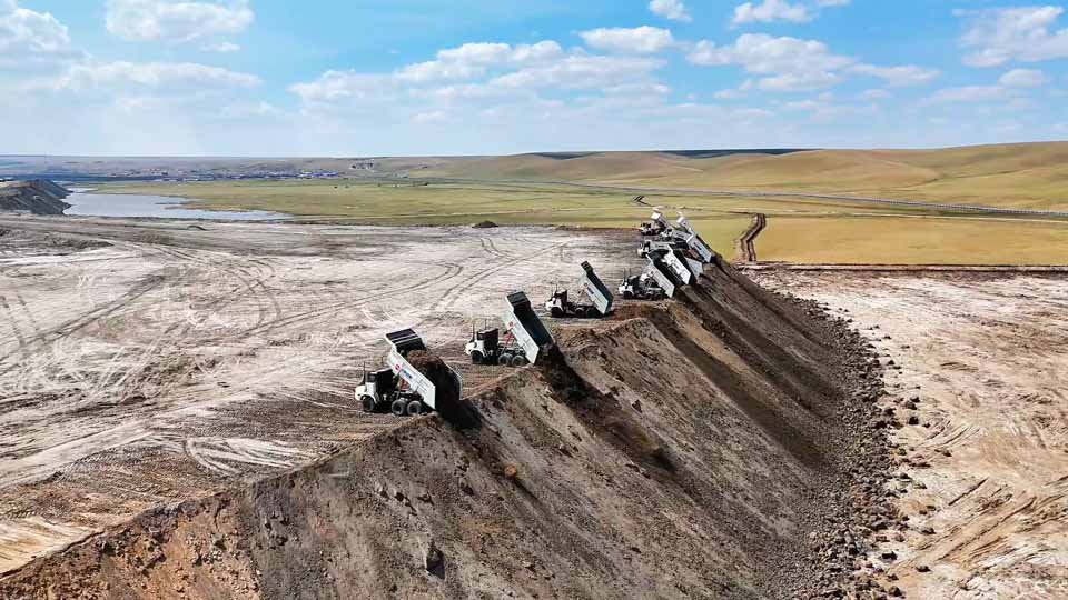 AI 트럭 여러 대가 절벽 가장자리에 정렬하여 동시에 토사를 쏟아내는 모습